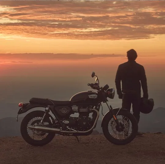 Motard contemplant le coucher de soleil à côté de sa Triumph Bonneville