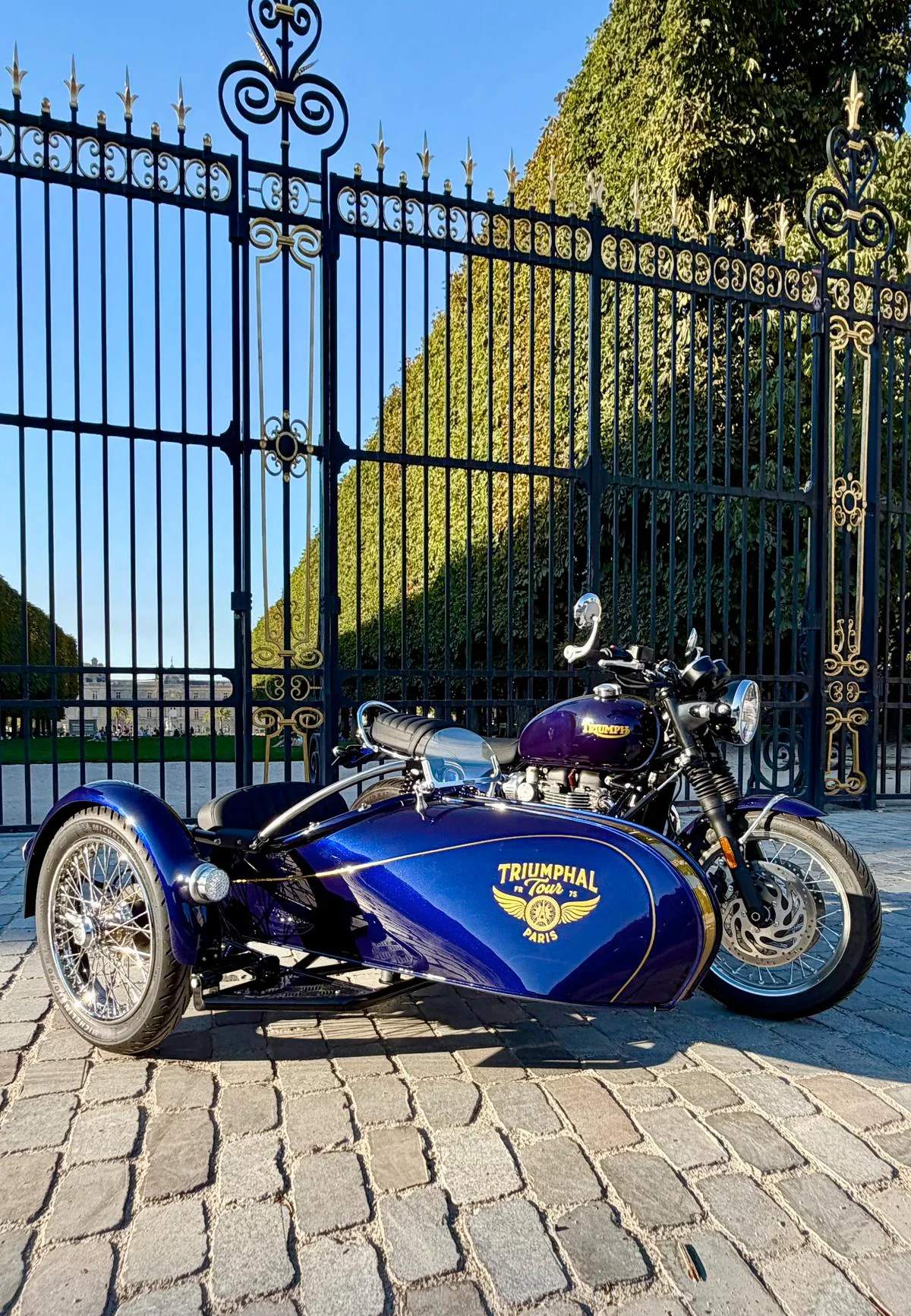 Blue Triumph sidecar of the Royal Escape in front of golden royal gates